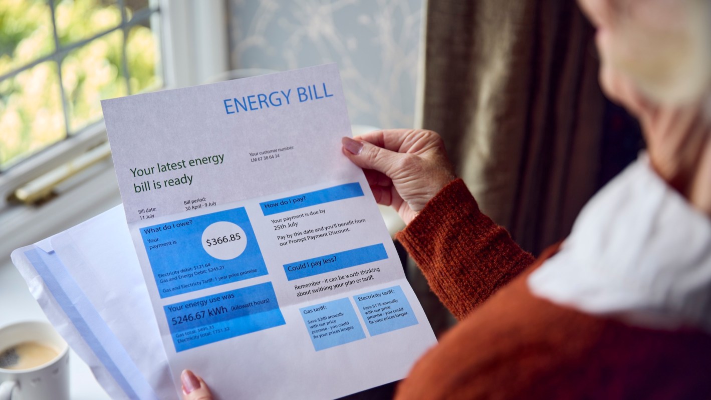 A person holding an energy bill with details about charges and payment options near a window.