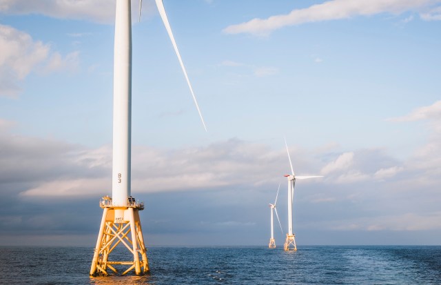 Three wind turbines stand in the ocean under a partly cloudy sky.