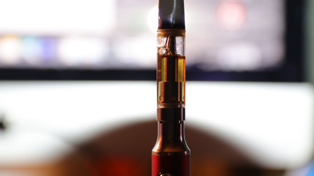 A close-up of a vape pen with a clear cartridge filled with golden liquid, set against a blurred background.