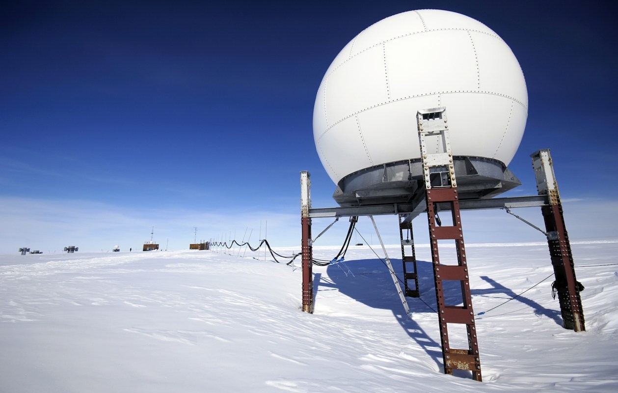 A white radar dome on a snowy landscape under a clear blue sky.