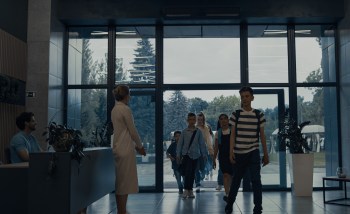 A group of children enters a school building while an adult stands at the reception area.