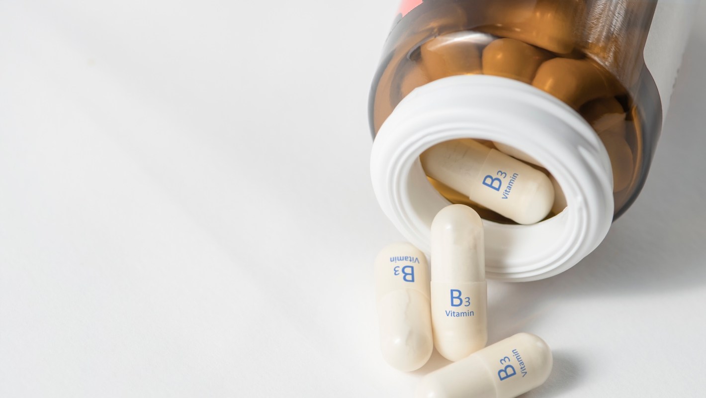 A brown bottle of Vitamin B3 capsules tipped over with several capsules on a white surface.