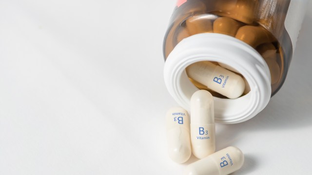 A brown bottle of Vitamin B3 capsules tipped over with several capsules on a white surface.