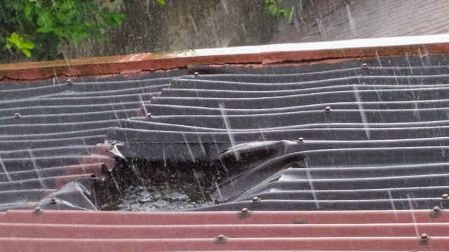 A damaged roof with water pooling in it amid heavy rain.
