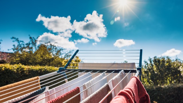 Clothes hanging on a drying rack under a bright blue sky with fluffy clouds and sunlight.