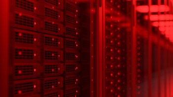 A row of data storage servers illuminated by red lights in a dimly lit environment.