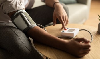 A person measures their blood pressure using an automatic monitor at a wooden table.