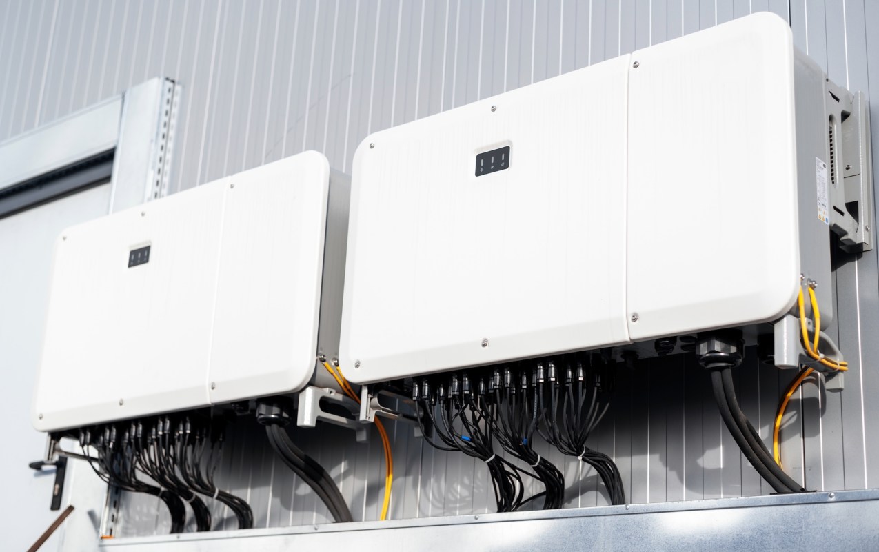 Two white solar inverters mounted on a wall, connected by multiple cables.