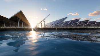 A solar panel farm reflected in calm water under a clear blue sky at sunset.