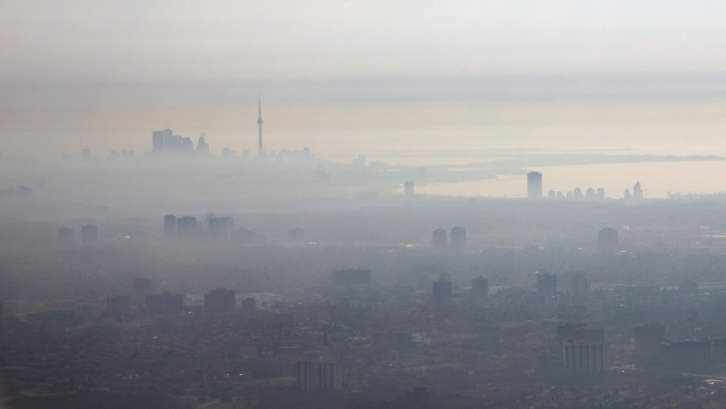 A hazy skyline of Toronto with a prominent tower, enveloped in fog and smog, against a muted sky.