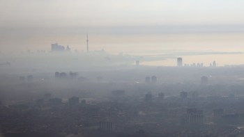 A hazy skyline of Toronto with a prominent tower, enveloped in fog and smog, against a muted sky.