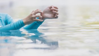 A person in gently rippling water uses one hand to scratch the other.