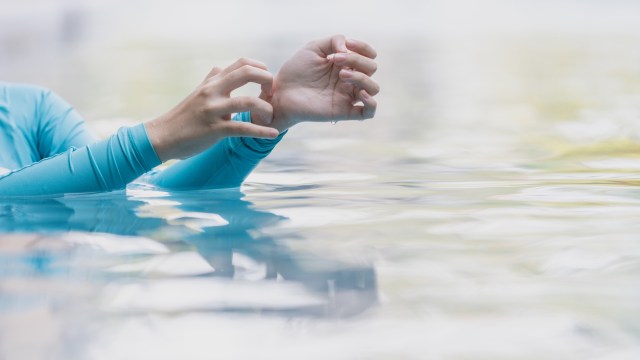 A person in gently rippling water uses one hand to scratch the other.
