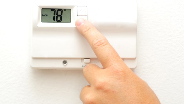 A person adjusts a digital thermostat displaying 78°F on a white wall.