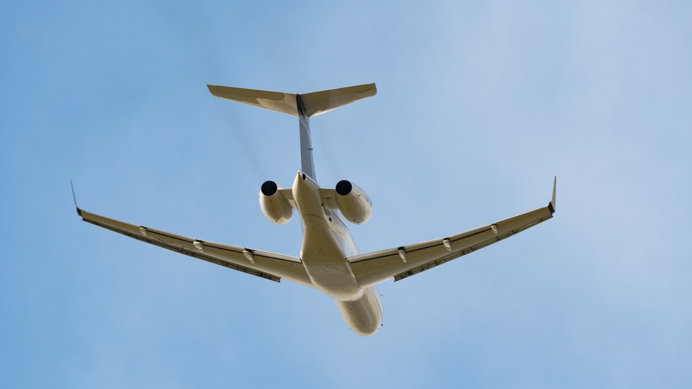 A private jet airplane flying overhead against a clear blue sky with slightly dark streamers out of its engine.