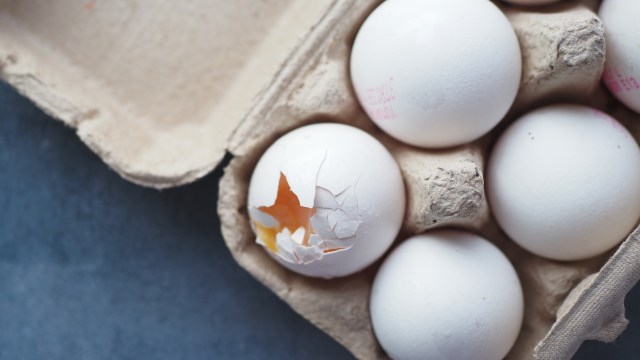 A close-up of an egg carton with several white eggs, one showing a cracked shell and visible yolk.