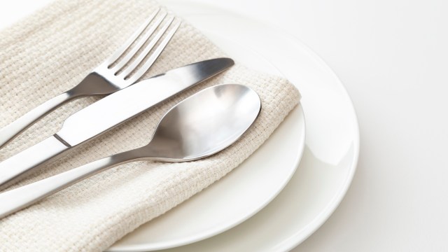 A plate set with a knife, fork, and spoon resting on a beige cloth napkin.