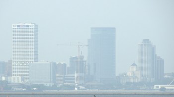 A skyline view of Milwaukee with tall buildings and a construction crane, shrouded in haze.