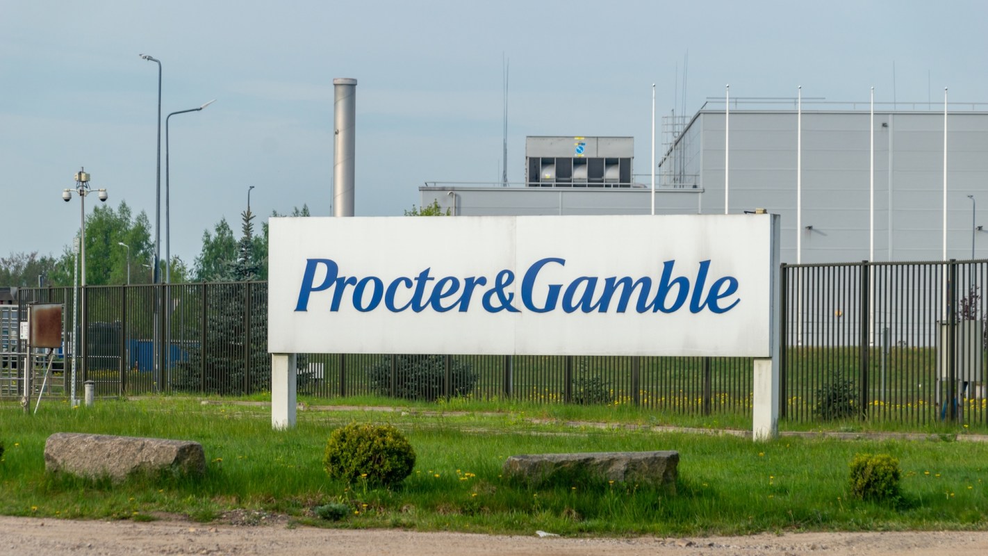 A sign for Procter & Gamble located near a factory, surrounded by grass and low shrubs.
