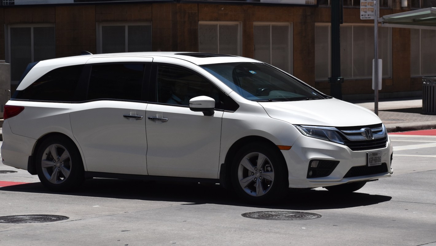 A white Honda Odyssey minivan goes through a city intersection .