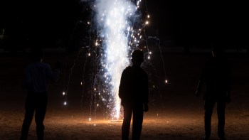 Three children silhouetted against a bright fountain firework illuminating a dark outdoor setting.