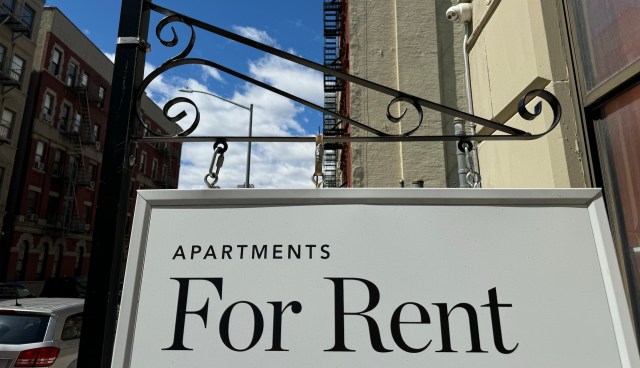 A sign reading "Apartments For Rent" hangs outside a building under a blue sky with clouds.