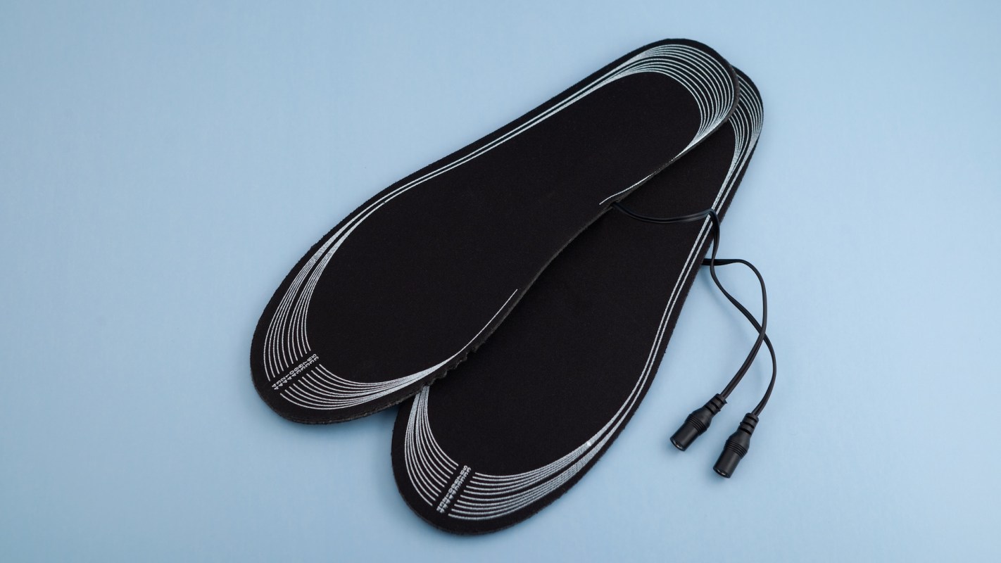 Two black heated insoles with white outlines and wired connectors, resting on a light blue background.