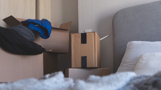 A cluttered bedroom corner with stacked cardboard boxes and a blue jacket hanging over the edge.