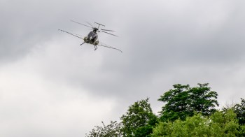 A helicopter flying above lush green trees under a cloudy sky.