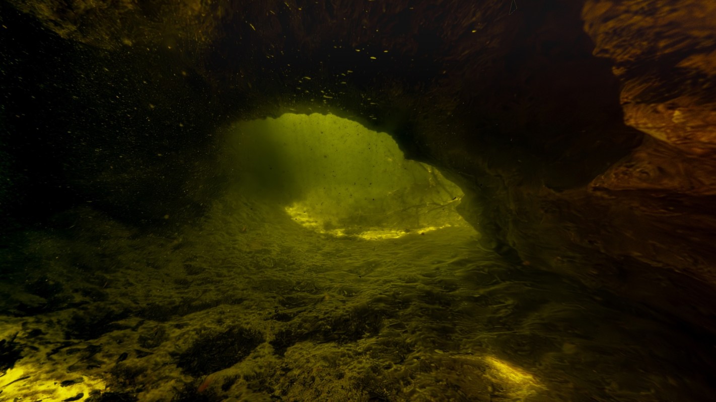 An underwater cave illuminated by a greenish light, showing swirling water and rocky textures.