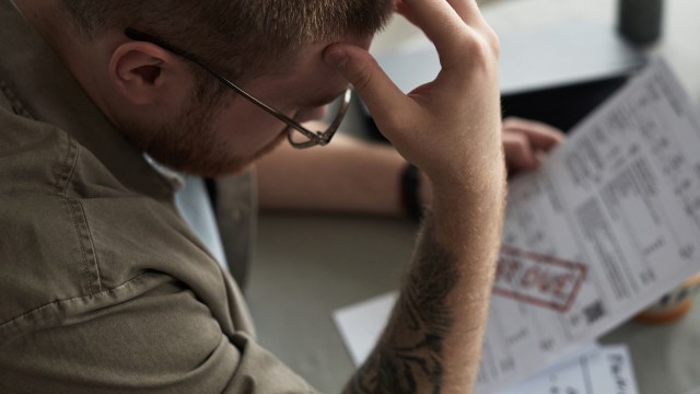A man with glasses holds his head while reviewing a past-due bill.