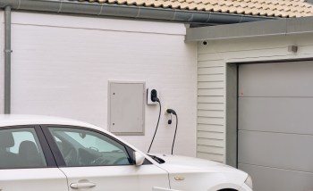 A white car parked next to a wall-mounted electric vehicle charger and a garage door.
