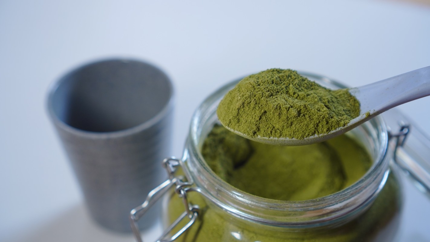 Green Moringa powder being scooped from a glass jar.