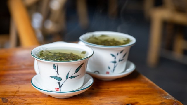 Two cups of steaming green tea sit on a wooden table, adorned with delicate leaf designs.