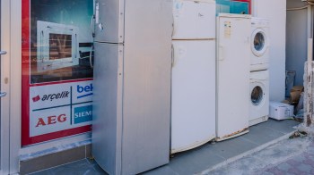A row of appliances including two refrigerators and a washing machine displayed outside a store front.