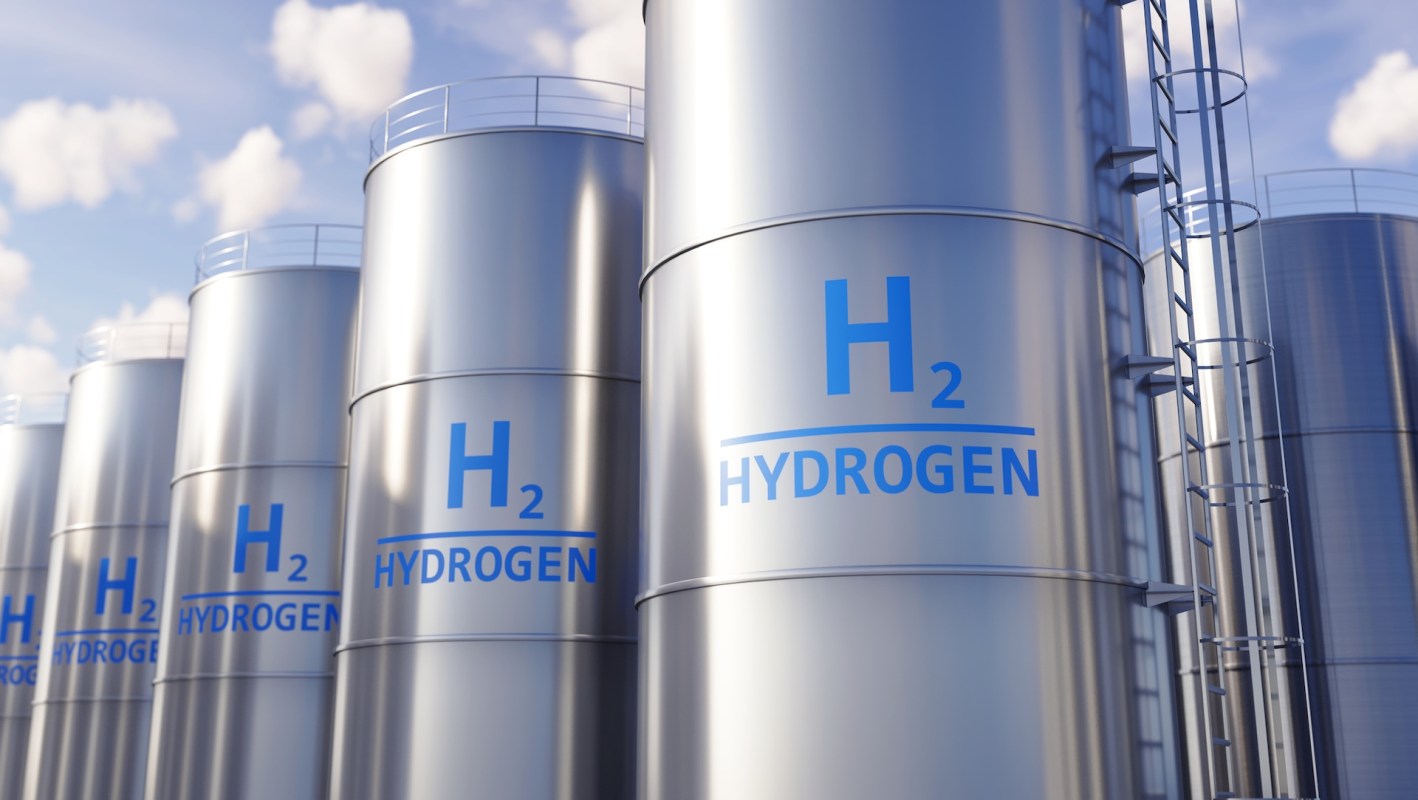 Row of metallic hydrogen storage tanks with blue "H2" and "HYDROGEN" labels against a cloudy sky.