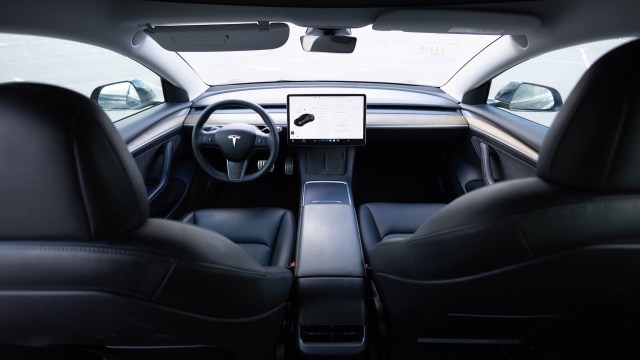 A sleek interior of a Tesla vehicle featuring a large touchscreen display and leather seats.