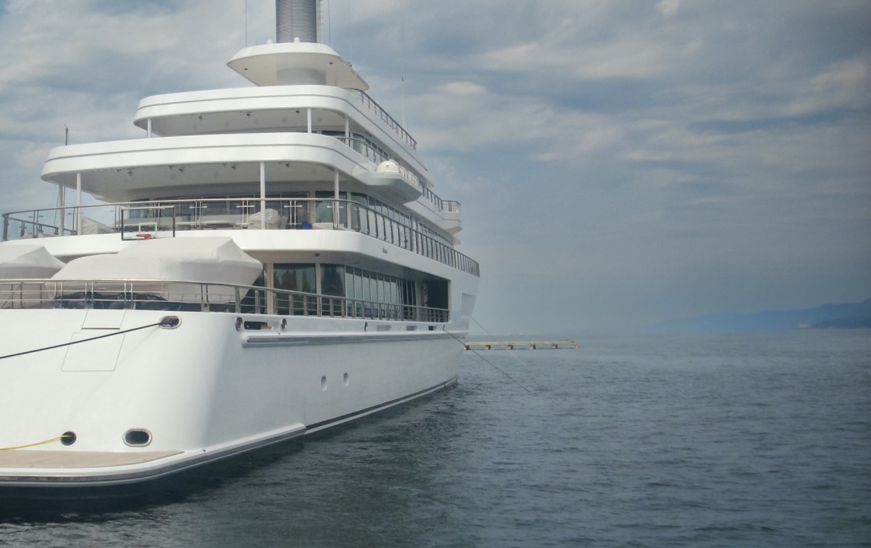 A luxurious white yacht anchored in calm waters with distant mountains under a cloudy sky.