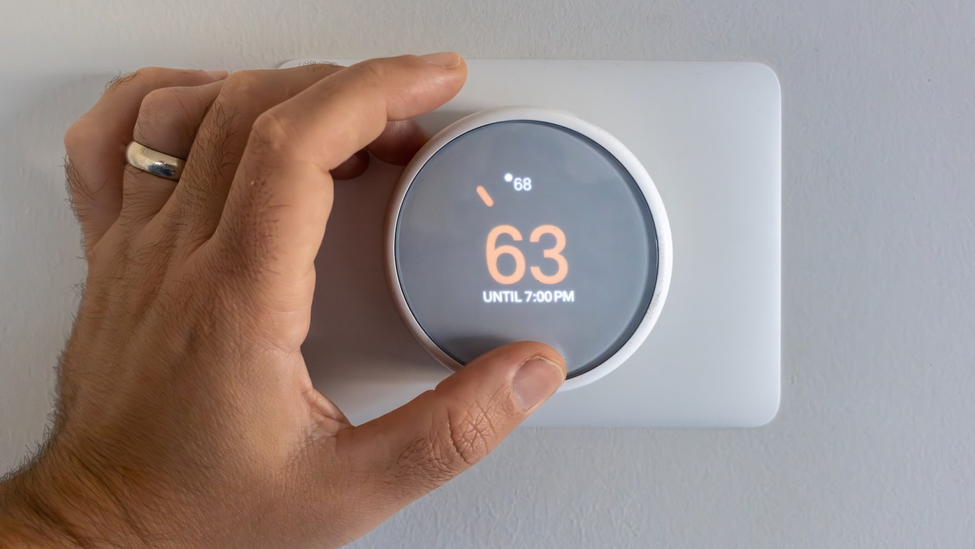 A hand adjusts a smart thermostat displaying a temperature of 63°F until 7 p.m.
