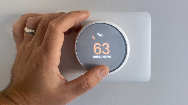 A hand adjusts a smart thermostat displaying a temperature of 63°F until 7 p.m.