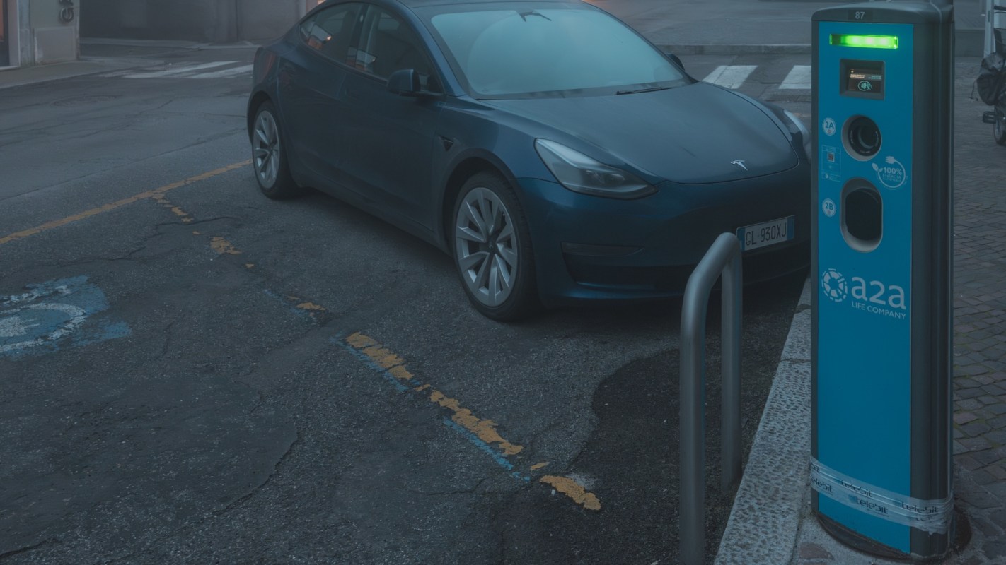A blue electric car parked next to a charging station on a dark city street.