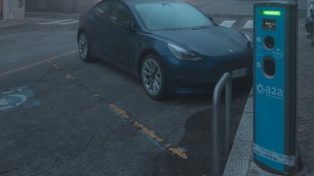 A blue electric car parked next to a charging station on a dark city street.