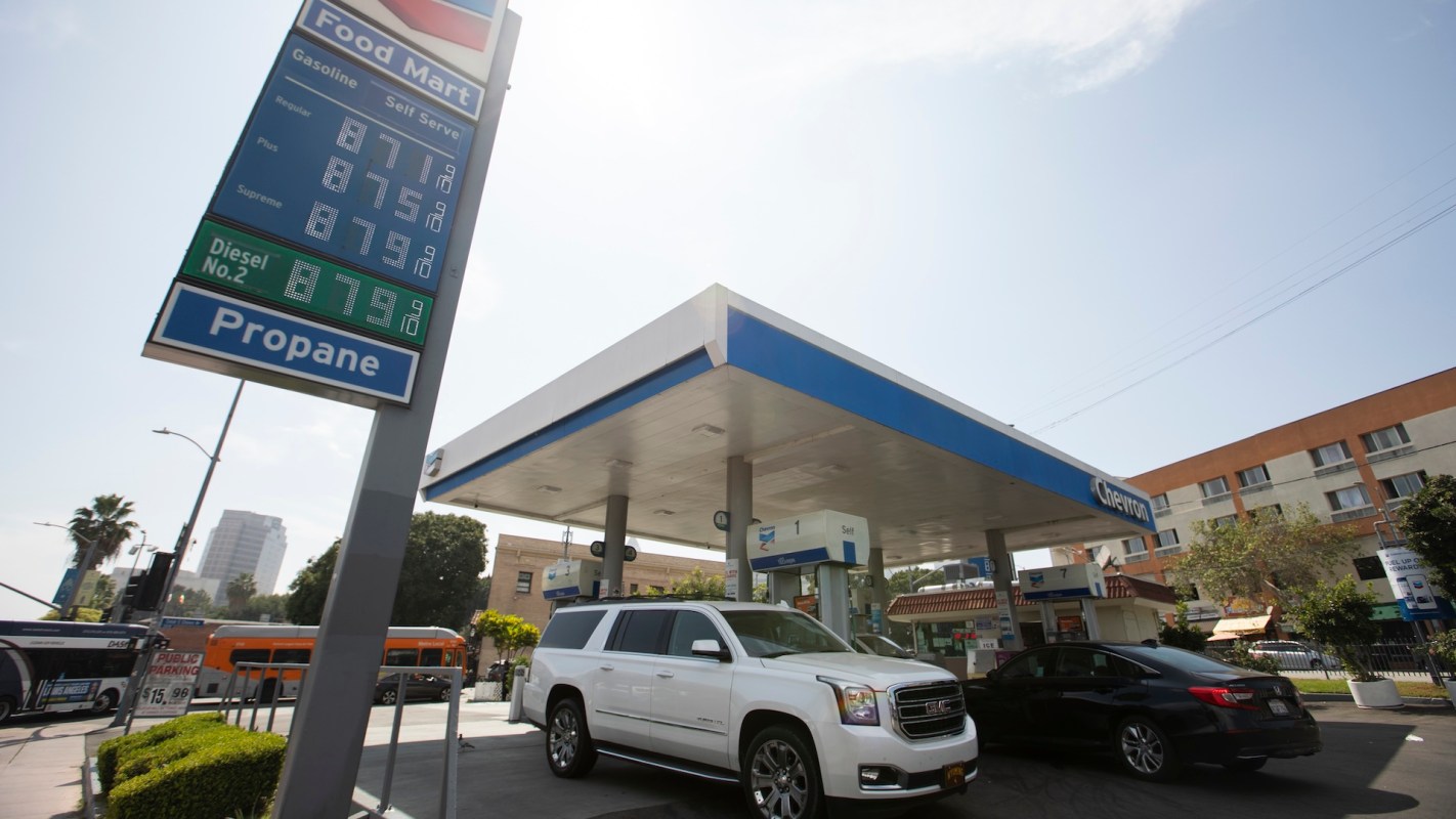 Two cars at a Chevron gas station with fuel prices at over $8.70 per gallon.