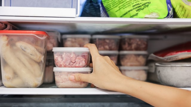 A hand reaching for containers of meat in a well-stocked freezer with frozen foods in the background.