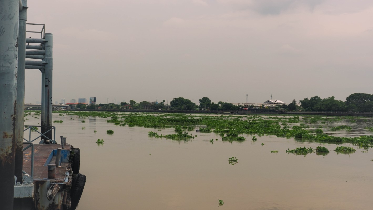 A dark orange river scene with lush greenery and distant buildings under an overcast sky.