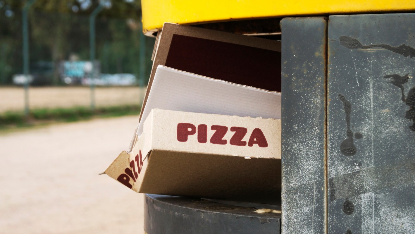 A pizza box poking out from a metal trash can.