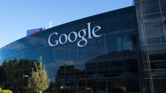 A close-up view of the Google logo on a modern glass building against a clear blue sky.