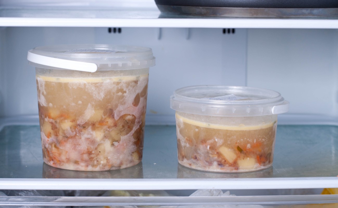 Two containers of frozen soup with visible ingredients, stored in a refrigerator.