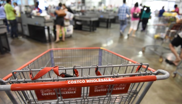 A shopping cart labeled "Costco Wholesale" in a busy supermarket checkout area.