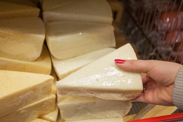 A hand holds a wedge of cheese surrounded by other pieces of cheese in a grocery store display.